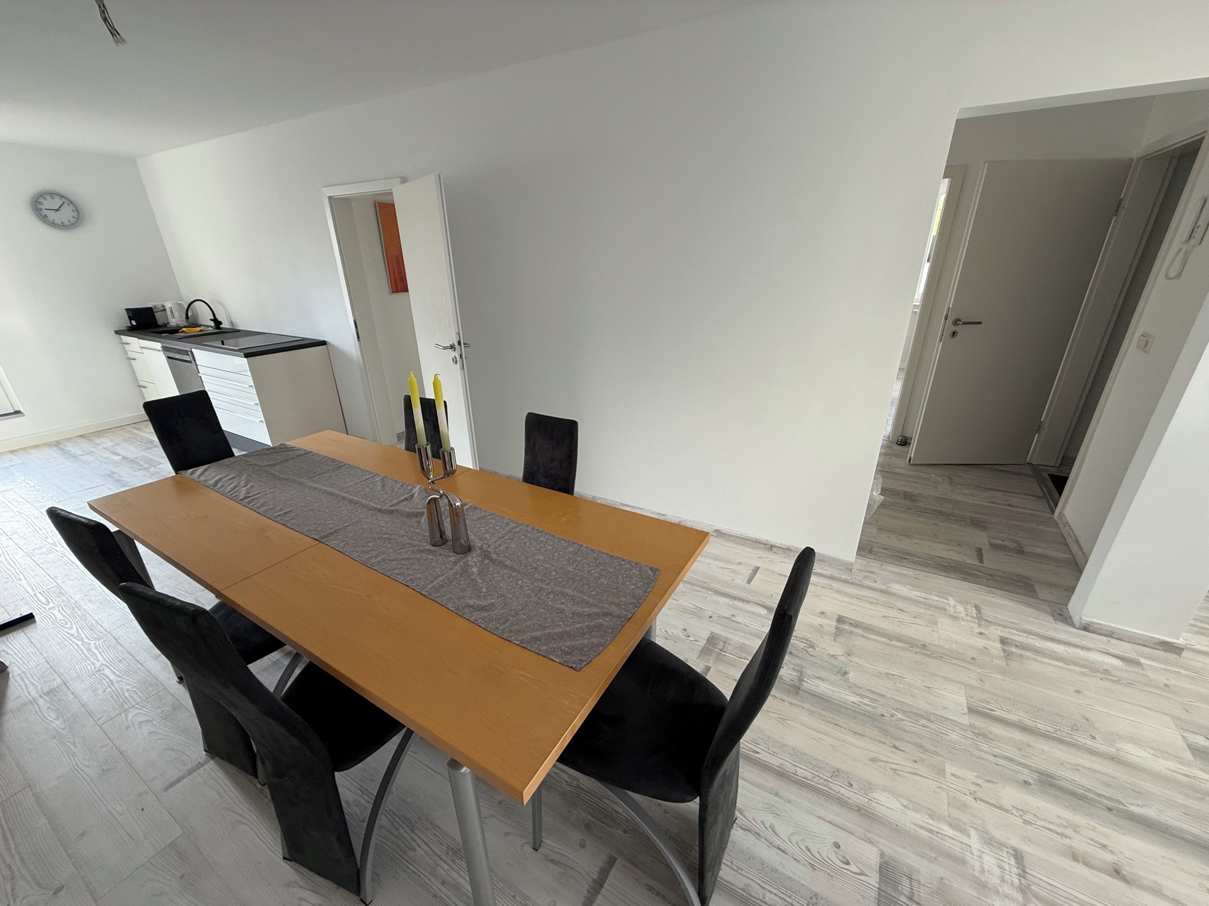 Un coin repas avec une table en bois, des chaises noires, un set de table gris et deux bougies.