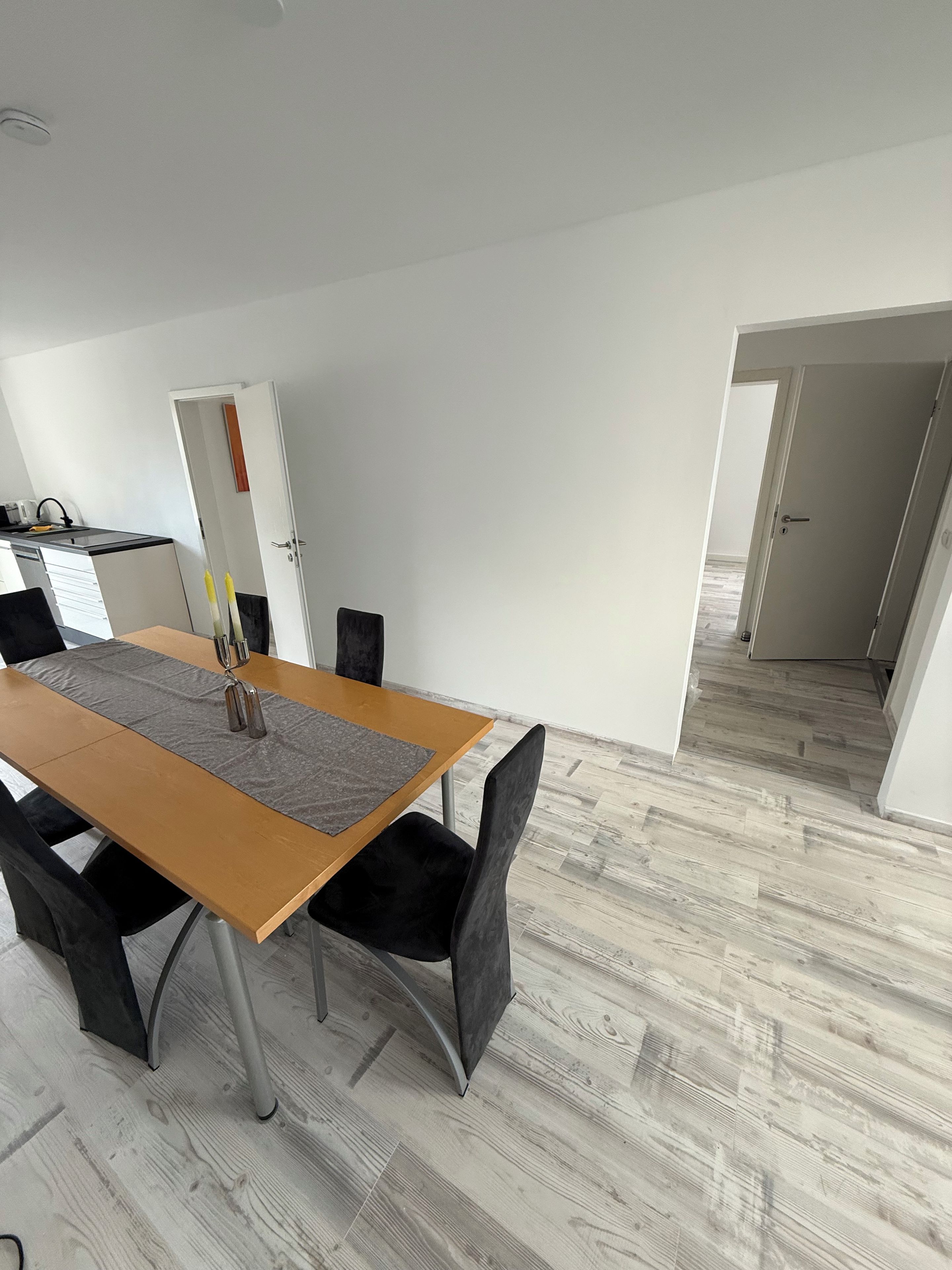 Un comedor con mesa de madera, sillas negras y un camino de mesa gris.