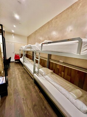 A bunk bed room with wooden flooring, a desk with a chair, and a red chair. - Dam Hotel (Amsterdam)