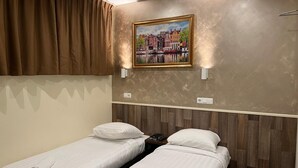 Una camera d'albergo con due letti singoli, un quadro che raffigura una città e una testiera in legno.