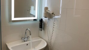 Un bagno con un lavandino bianco, uno specchio illuminato e un asciugacapelli montato a parete.