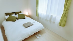 A neatly made bed with pillows, a folded towel, and slippers on the floor. - MSTAY Takadanobaba One (Shinjuku-ku)