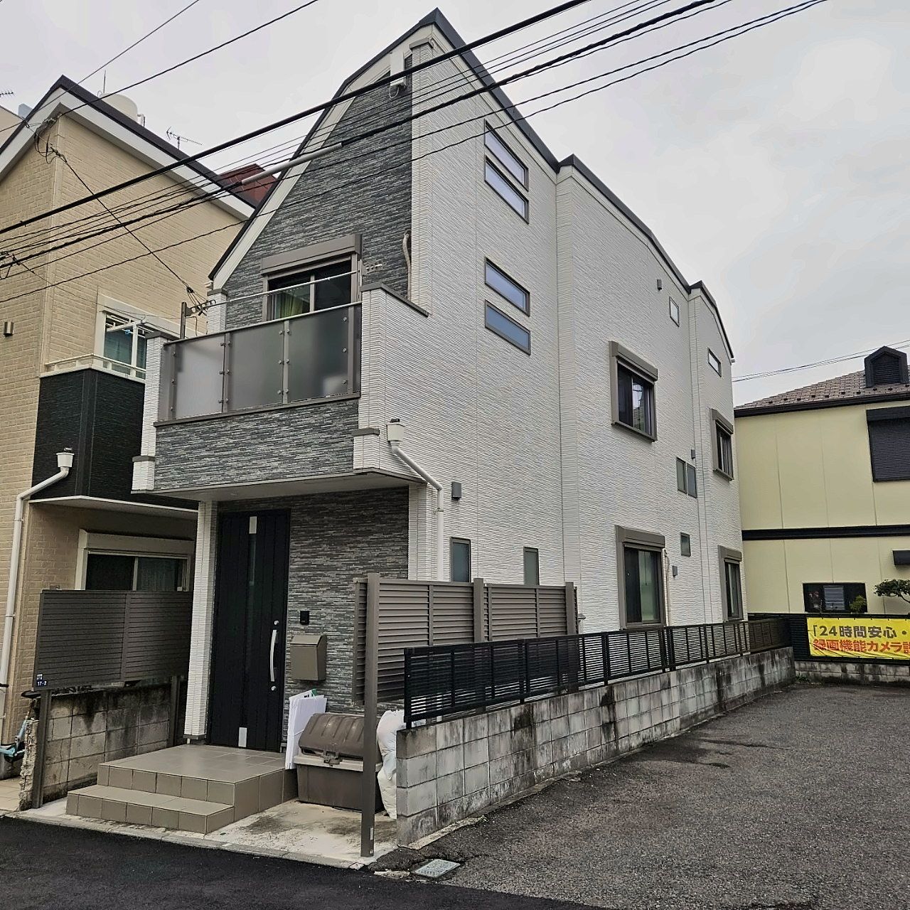 Un immeuble résidentiel de deux étages doté d’un balcon, d’une porte de garage et d’un petit jardin à l’avant.