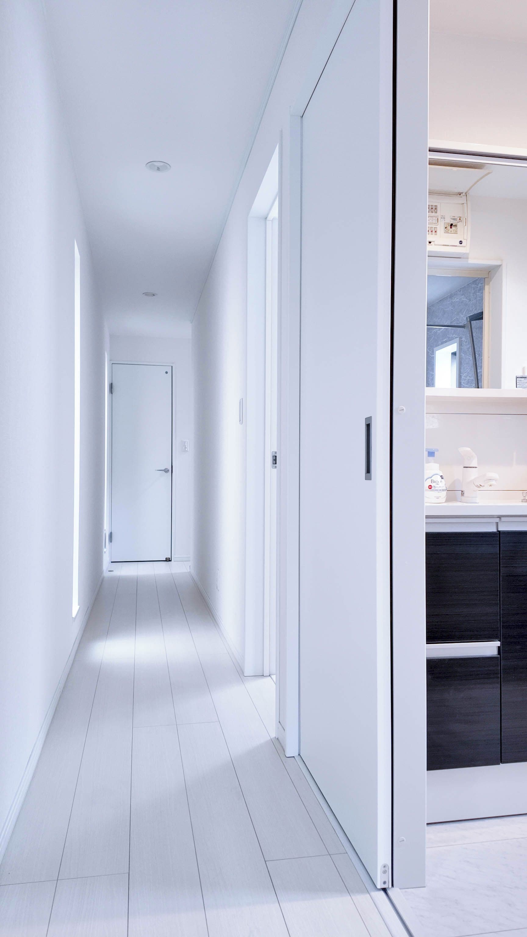 Een moderne, minimalistische hal met witte wanden en een betegelde vloer die naar een deur leidt.