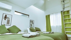 Une chambre d’hôtel avec deux lits, une literie verte, une lucarne et des œuvres d’art accrochées aux murs.