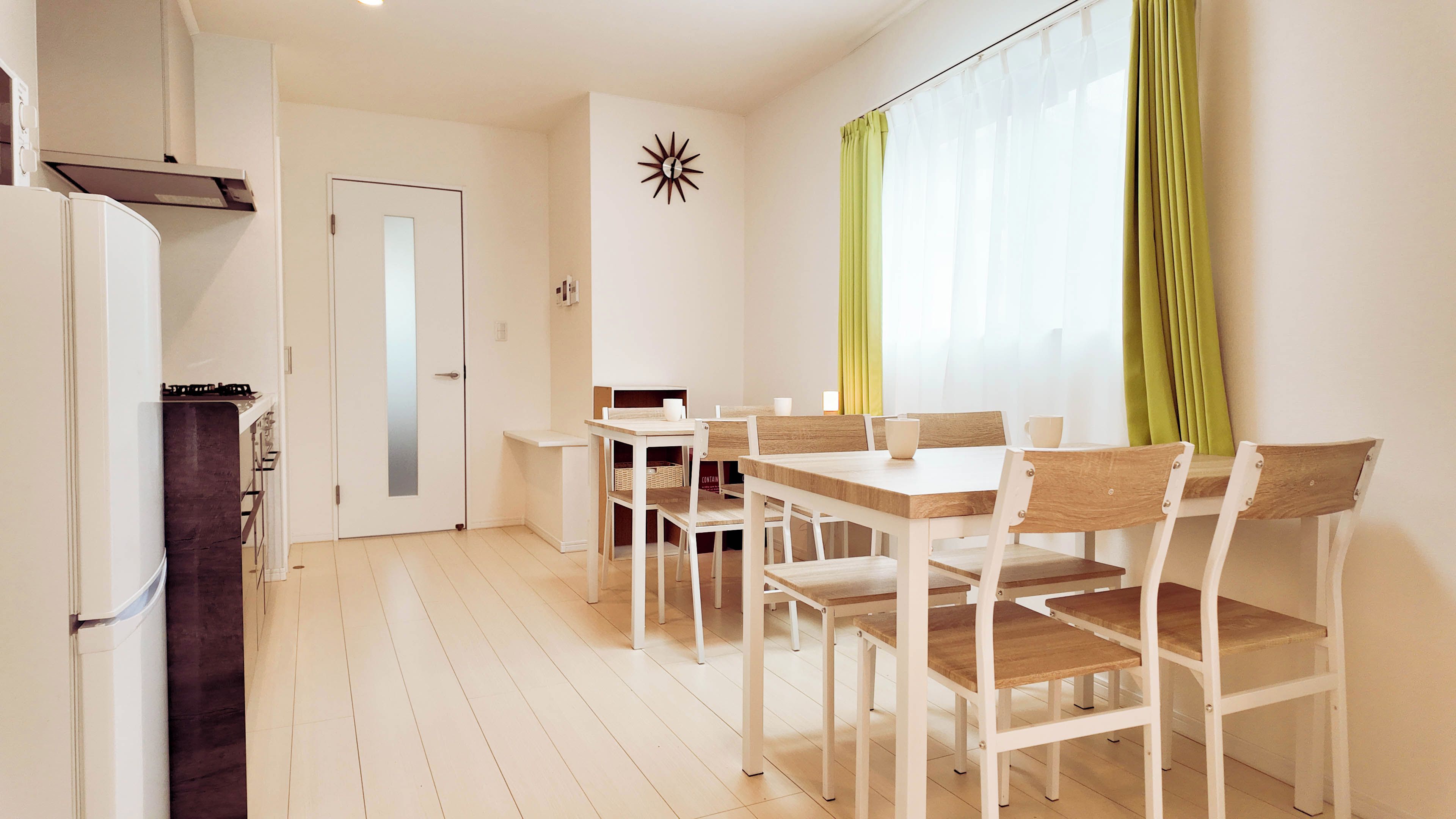 Un coin repas avec une table et des chaises, un coin cuisine avec un réfrigérateur, et une porte avec un miroir.
