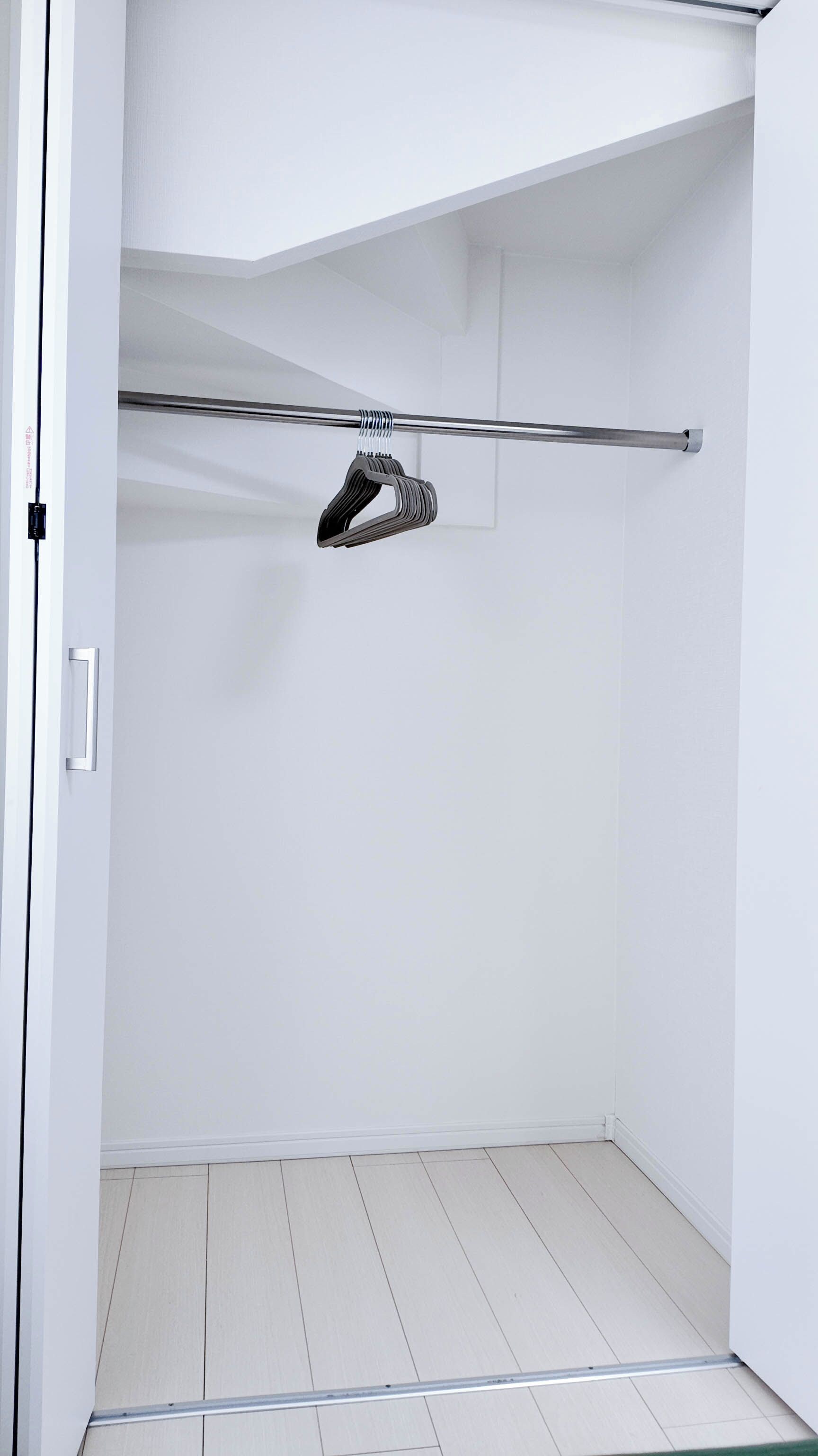 Un dressing avec une tringle métallique pour suspendre les vêtements, une porte blanche et un sol carrelé.