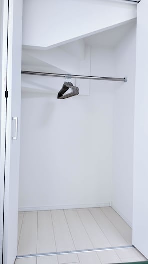 A walk-in closet with a metal rod for hanging clothes, a white door, and a tiled floor. - MSTAY Takadanobaba One (Shinjuku-ku)