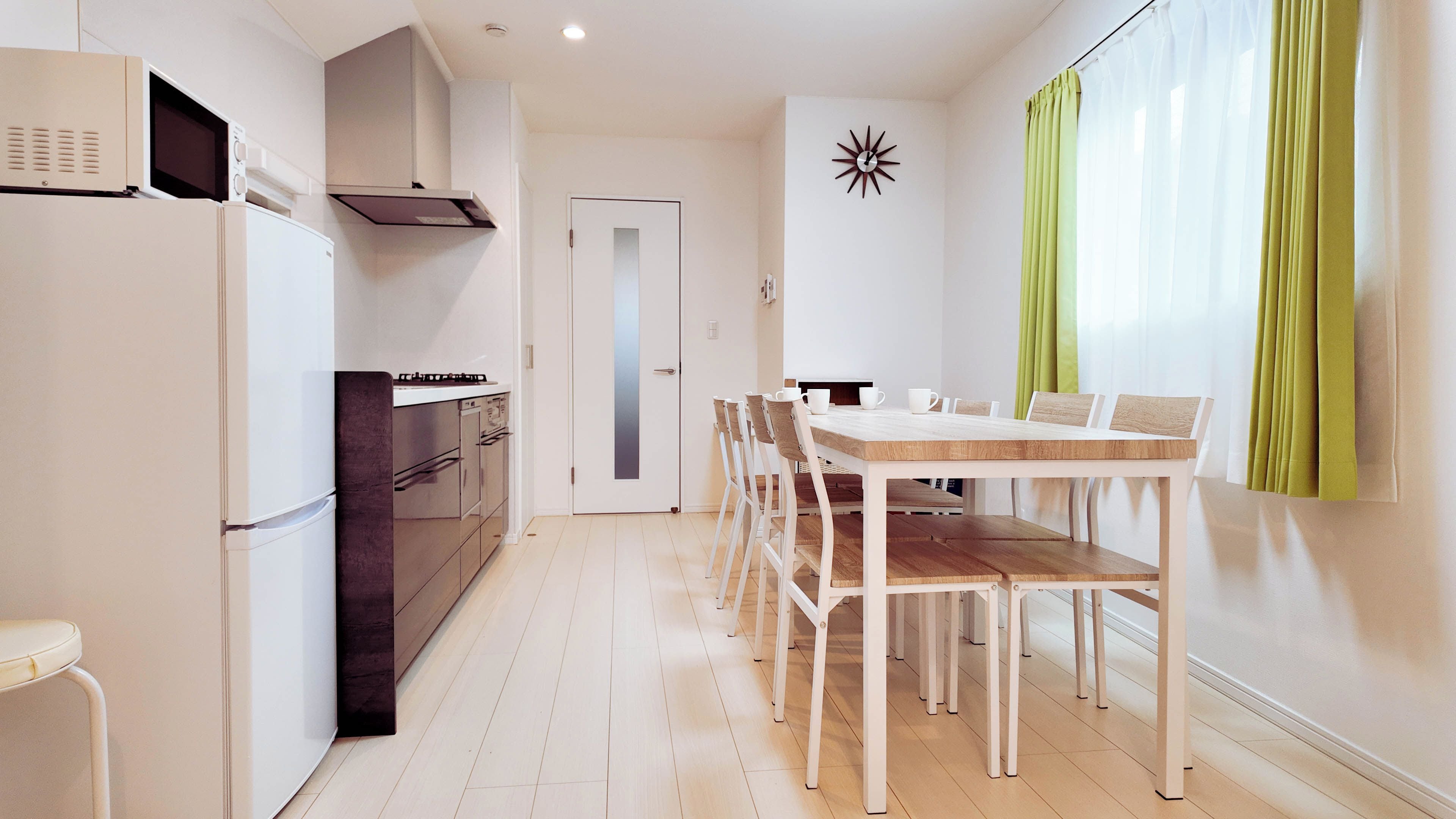 A modern kitchen with a dining area, white cabinetry, and a wooden table.