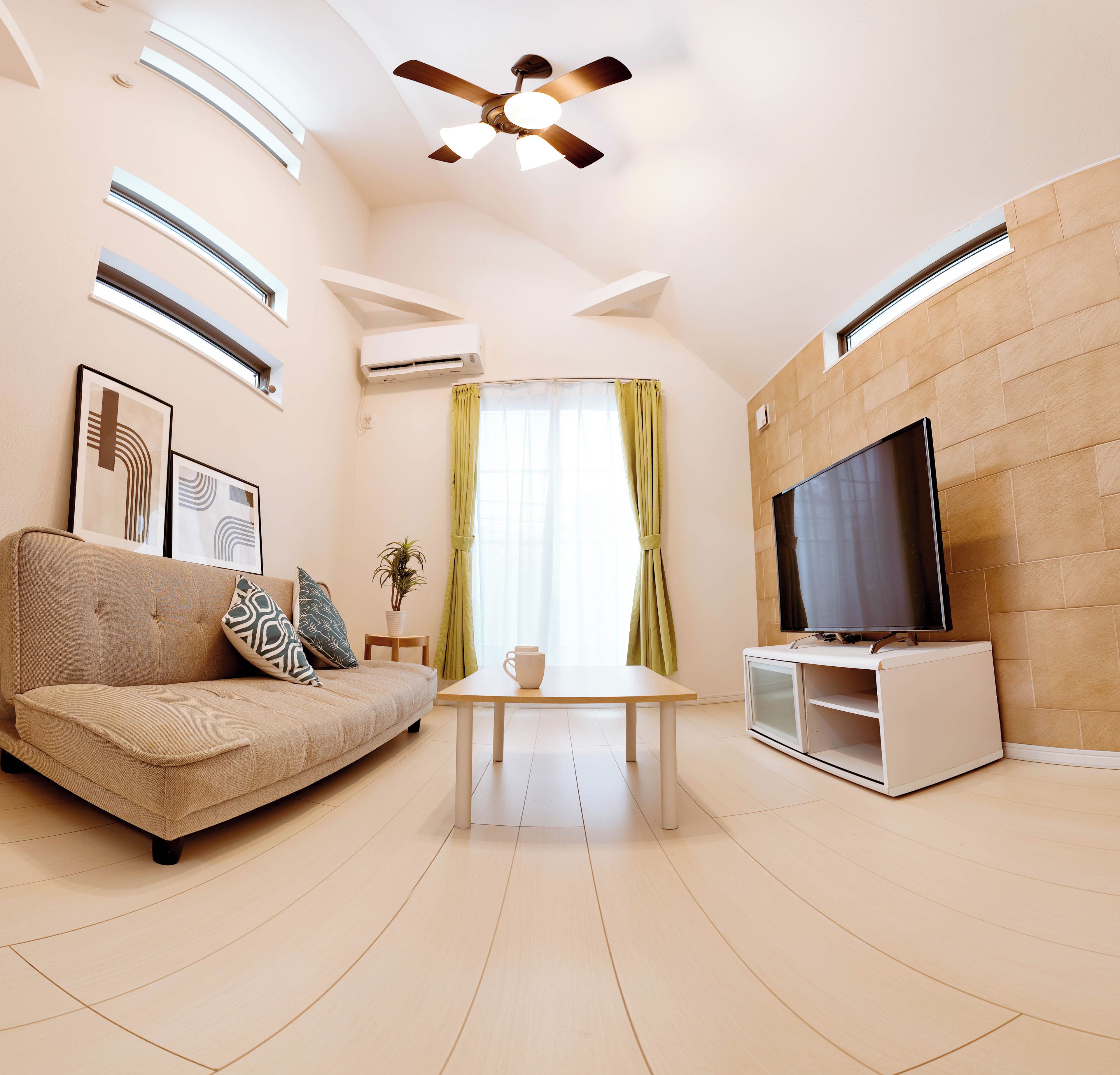 A modern living room with a sofa, a coffee table, a television, and a ceiling fan.