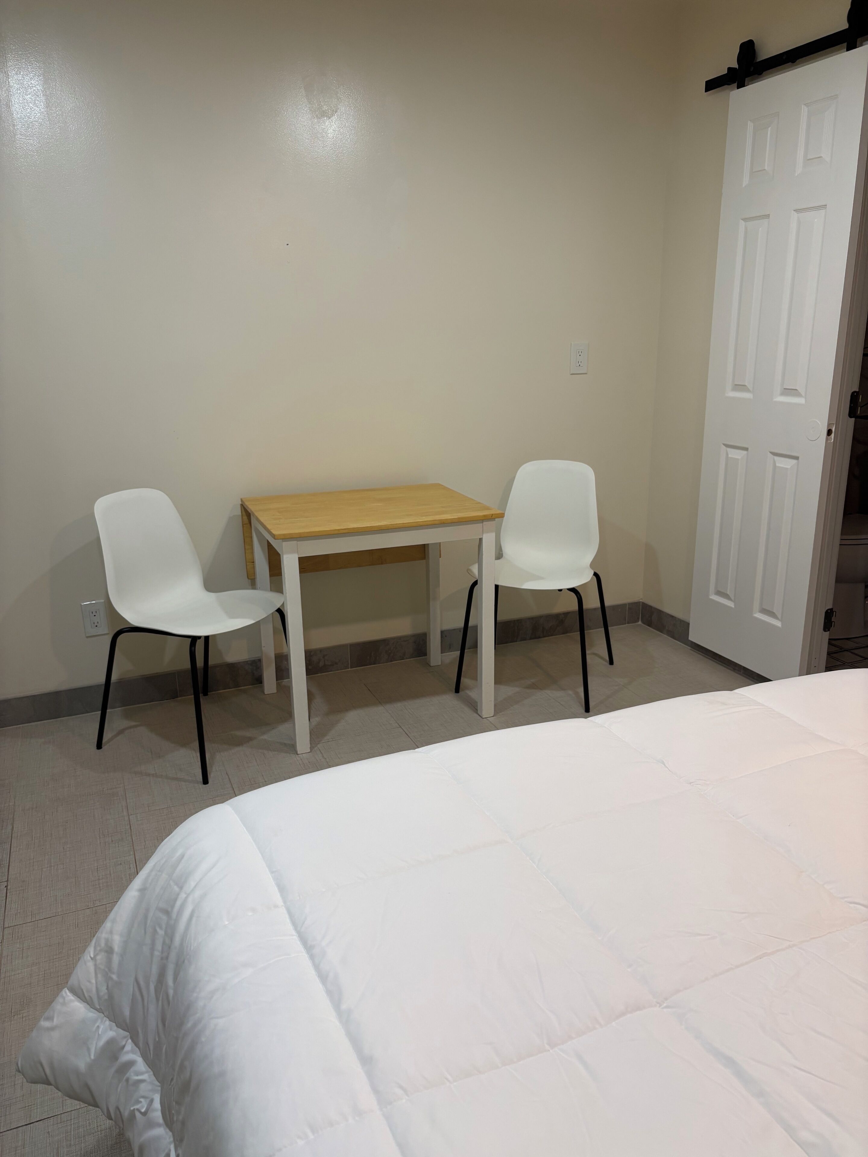 Um quarto com uma cama, uma mesa de madeira e duas cadeiras brancas.