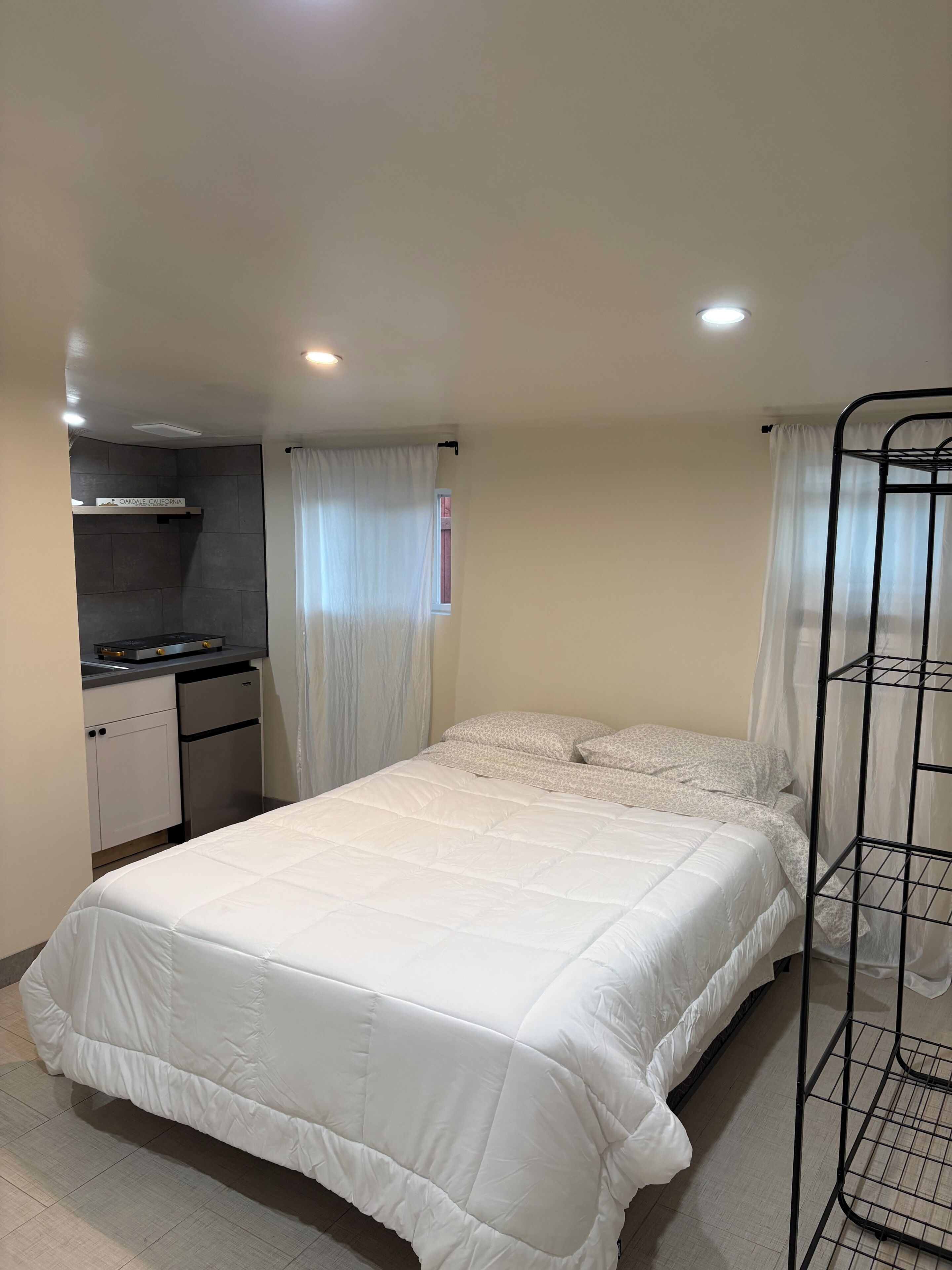 A bedroom with a bed, a bunk bed, a kitchenette, and a window with curtains.