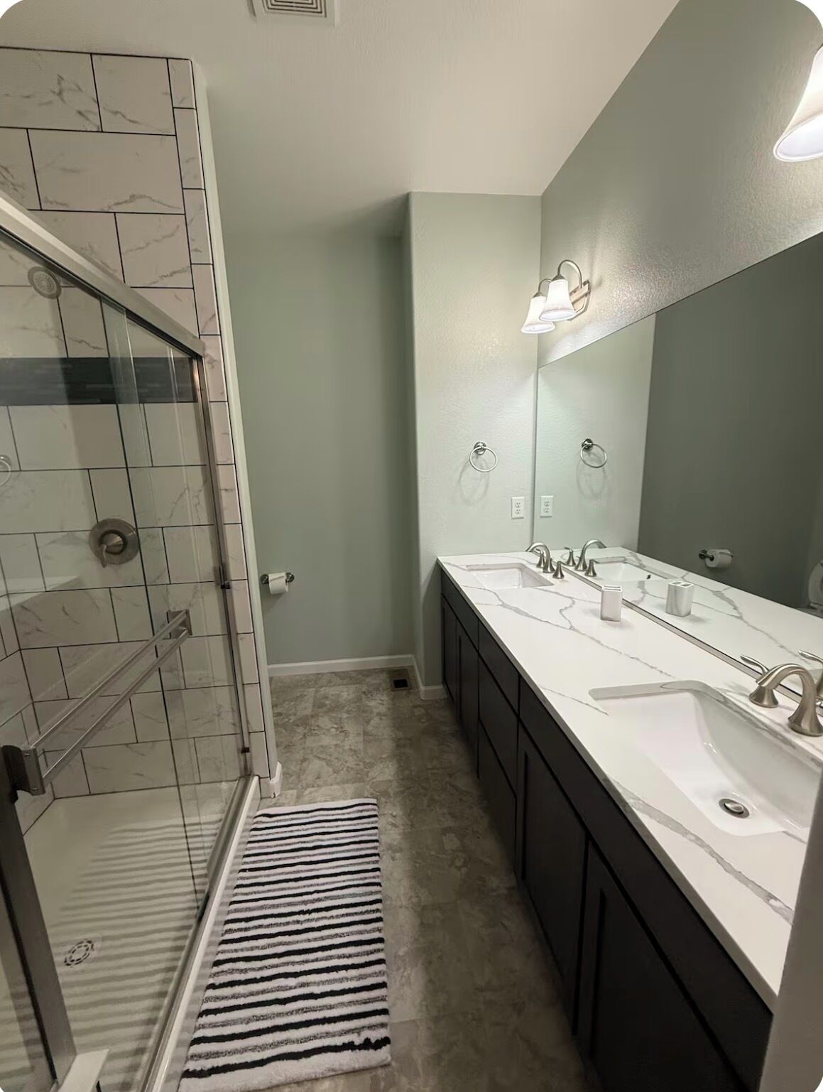 A bathroom with a glass shower enclosure, a double sink vanity, and a large mirror.
