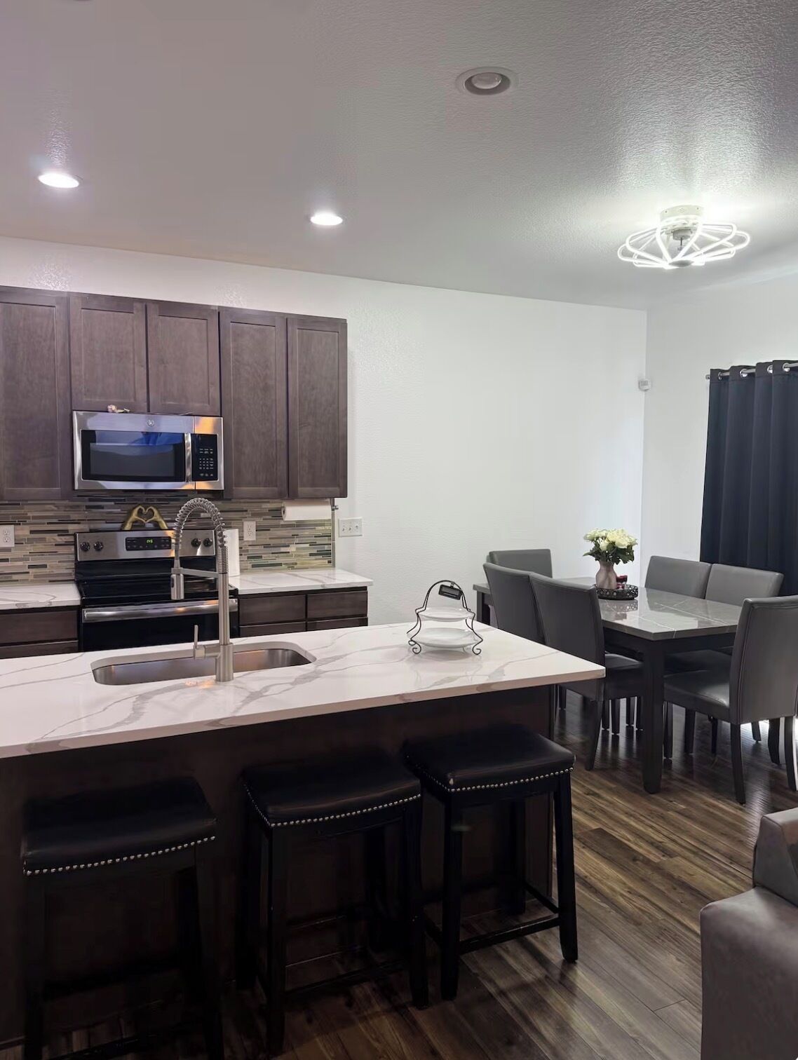 Una cocina moderna con alacenas de madera oscura, electrodomésticos de acero inoxidable, encimera de mármol y un comedor con mesa y sillas.
