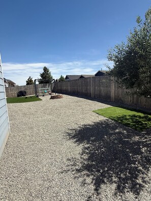 A gravel driveway leading to a wooden fence with a covered bench and a trampoline. - Charming Pet friendly 3-bedroom house with AC in Milliken (Milliken)