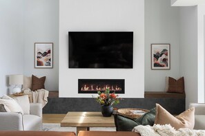 A modern living room with a fireplace, a flat-screen TV mounted on the wall, and two framed artworks. - Ember Rise | Daylesford 3BR, Fireplace, Sleeps 6 (Daylesford)