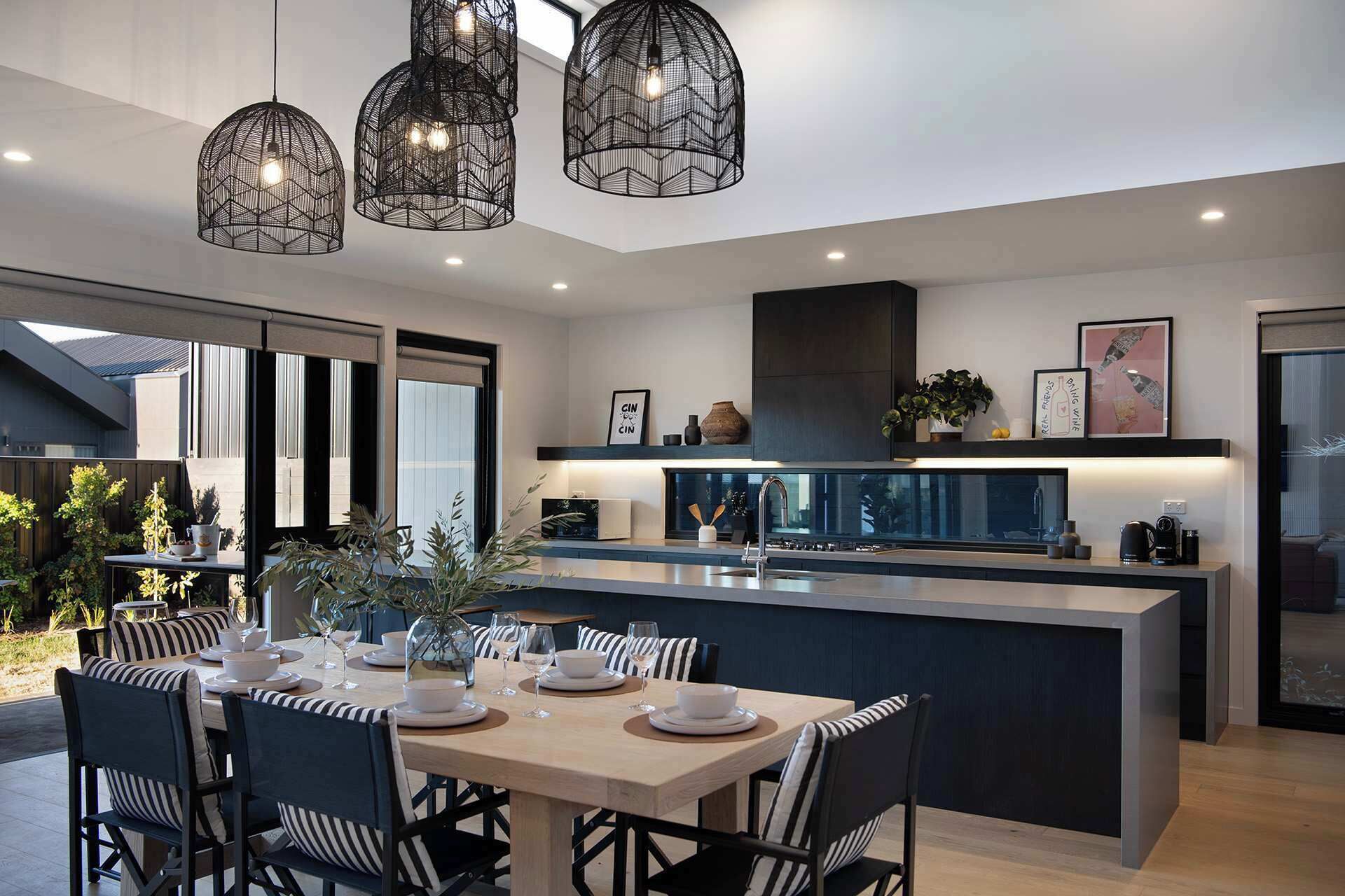 A modern kitchen with a central island, pendant lighting, and a dining area with striped chairs.