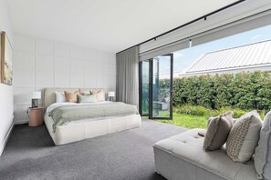 A modern bedroom with a large bed, a bedside table, and a view of a garden through a sliding glass door. - Ember Rise | Daylesford 3BR, Fireplace, Sleeps 6 (Daylesford)