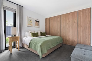 Un dormitorio con cama, mesita de noche, lámpara, ventana con cortinas y armario de madera.