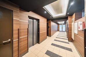 A modern hallway with wooden paneling, a tiled floor, and a ceiling with recessed lighting. - Apartment Hotel 11 Kuromon 7 (Osaka-shi)