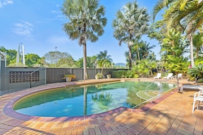 A swimming pool with a brick deck, surrounded by palm trees and a fence. - Esplanade Views with Pool, CBD (Cairns North)