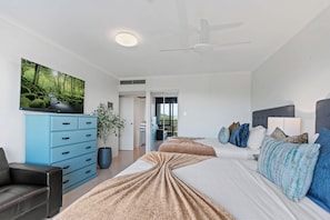 A modern bedroom with two beds, a blue dresser, a ceiling fan, and a large window. - Esplanade Views with Pool, CBD (Cairns North)