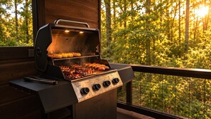 A barbecue grill with multiple cooking zones and a digital display, positioned on a balcony with a view of a forested area. - The Rustic Reserve – Luxury cabin with Hot Tub, Pool Table, Arcade & Stone Soaking Tub - Broken Bow, OK (Broken Bow)