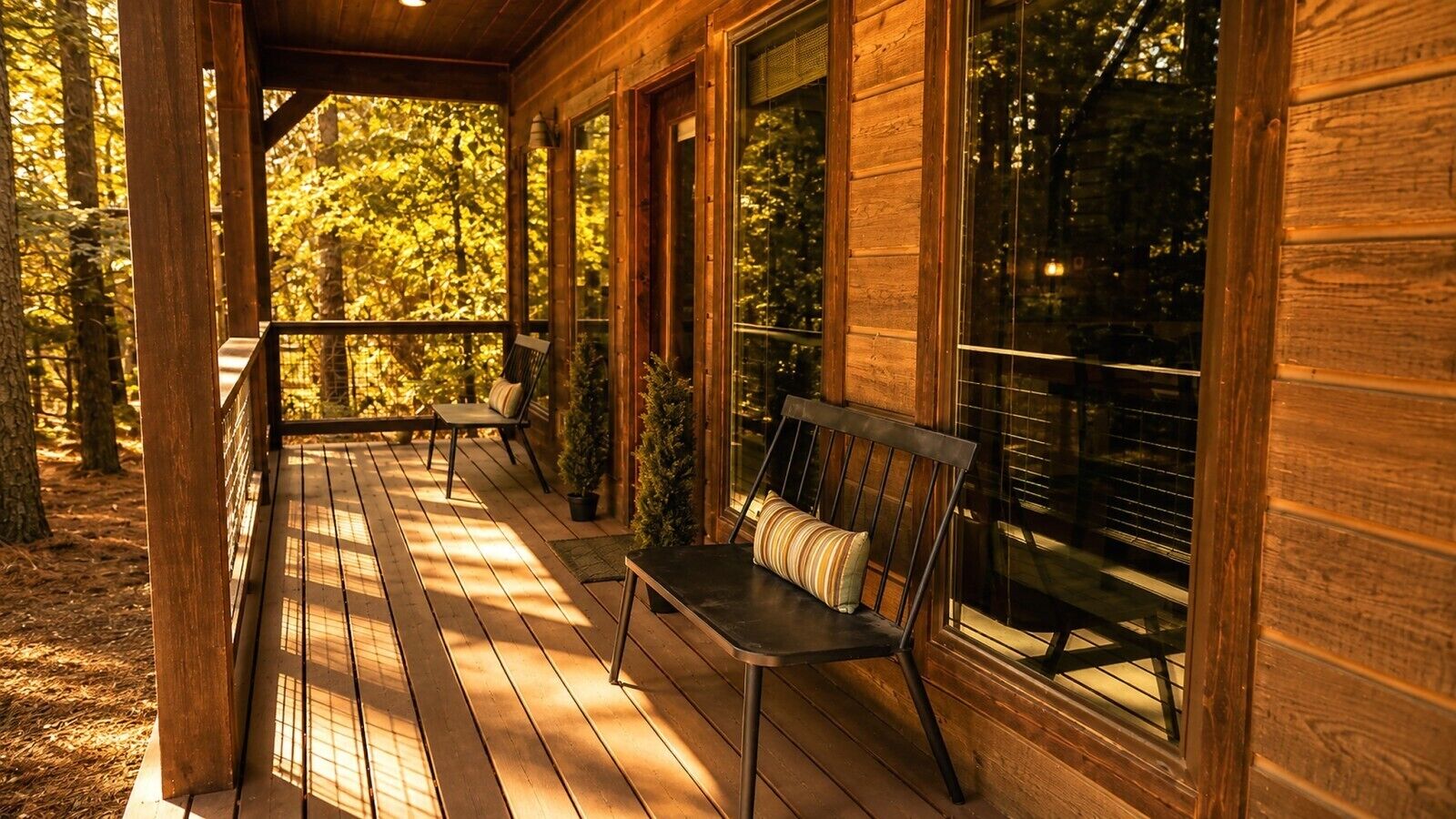 A wooden porch with a bench and potted plants, overlooking a forest.