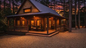 Une cabane en bois dotée d’une véranda, de grandes fenêtres et d’un espace aménagé pour faire un feu de camp.