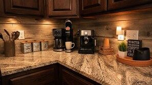 A kitchen counter with a coffee maker, a mug, and a sign that reads 'NO MATTER THE QUESTION COFFEE IS THE ANSWER'. - The Rustic Reserve – Luxury cabin with Hot Tub, Pool Table, Arcade & Stone Soaking Tub - Broken Bow, OK (Broken Bow)