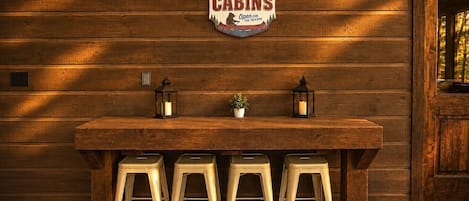 L’intérieur d’un chalet en bois, avec une pancarte indiquant « Les chalets au bord du lac sont ouverts pour la saison », un comptoir de bar en bois, quatre tabourets et deux lanternes.