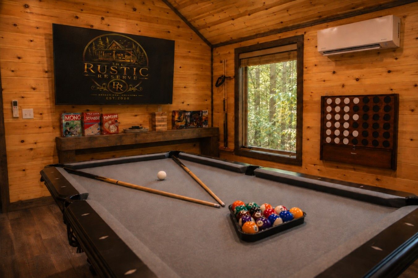 A pool table with a cue stick, pool balls, and a window with a view of trees.