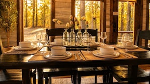 A dining table set for four with white plates, bowls, and glassware, flanked by chairs. - Luxury cabin w/ Hot Tub, Pool Table, Arcade & Stone Soaking Tub - Broken Bow, OK (Broken Bow)