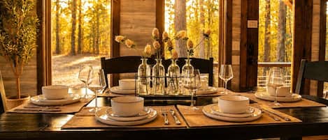 A dining table set for four with white plates, bowls, and glassware, flanked by chairs.