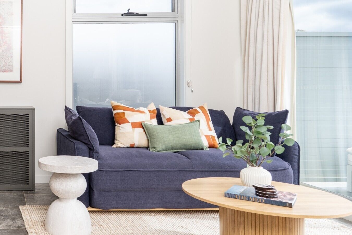 A modern living room with a dark blue sofa, a round wooden coffee table, and a white side table.