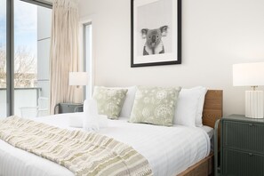 A hotel room with a bed, a framed picture of a koala, a window with curtains, and a nightstand with a lamp. - Quiet Turner Stay | Walk to Braddon & ANU (Turner)