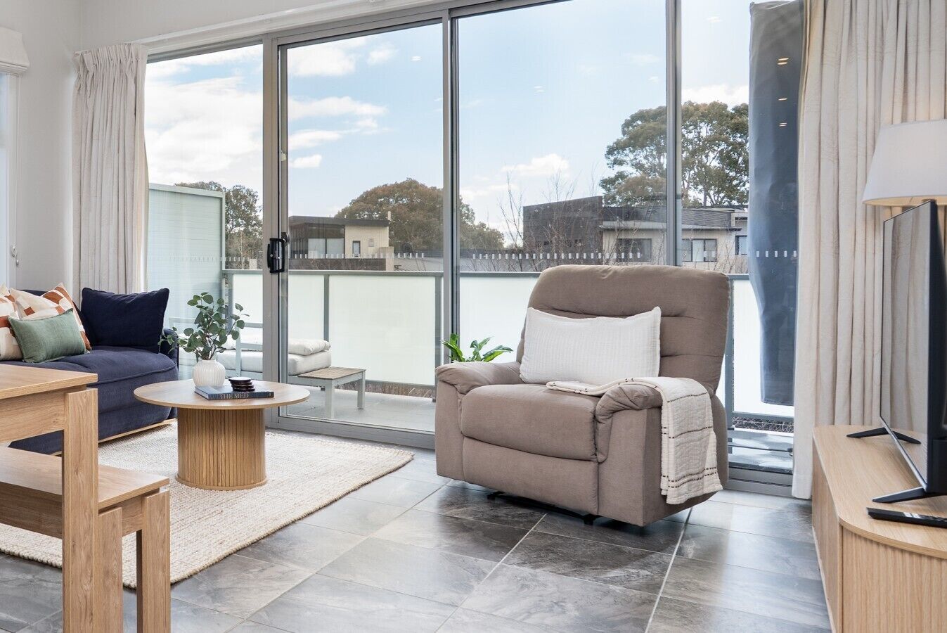 A modern living room with a sofa, armchair, coffee table, and a television.
