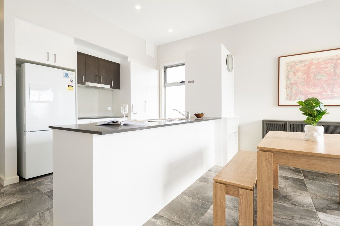 A modern kitchen with white cabinetry, a black countertop, and a wooden dining table.