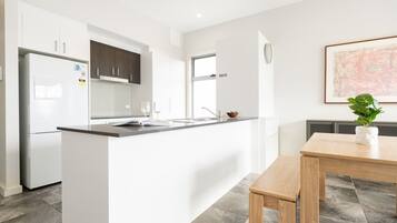 A modern kitchen with white cabinetry, a black countertop, and a wooden dining table.