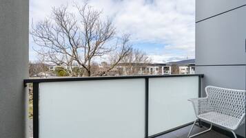A balcony with a white chair, a glass partition, and a view of leafless trees and buildings.