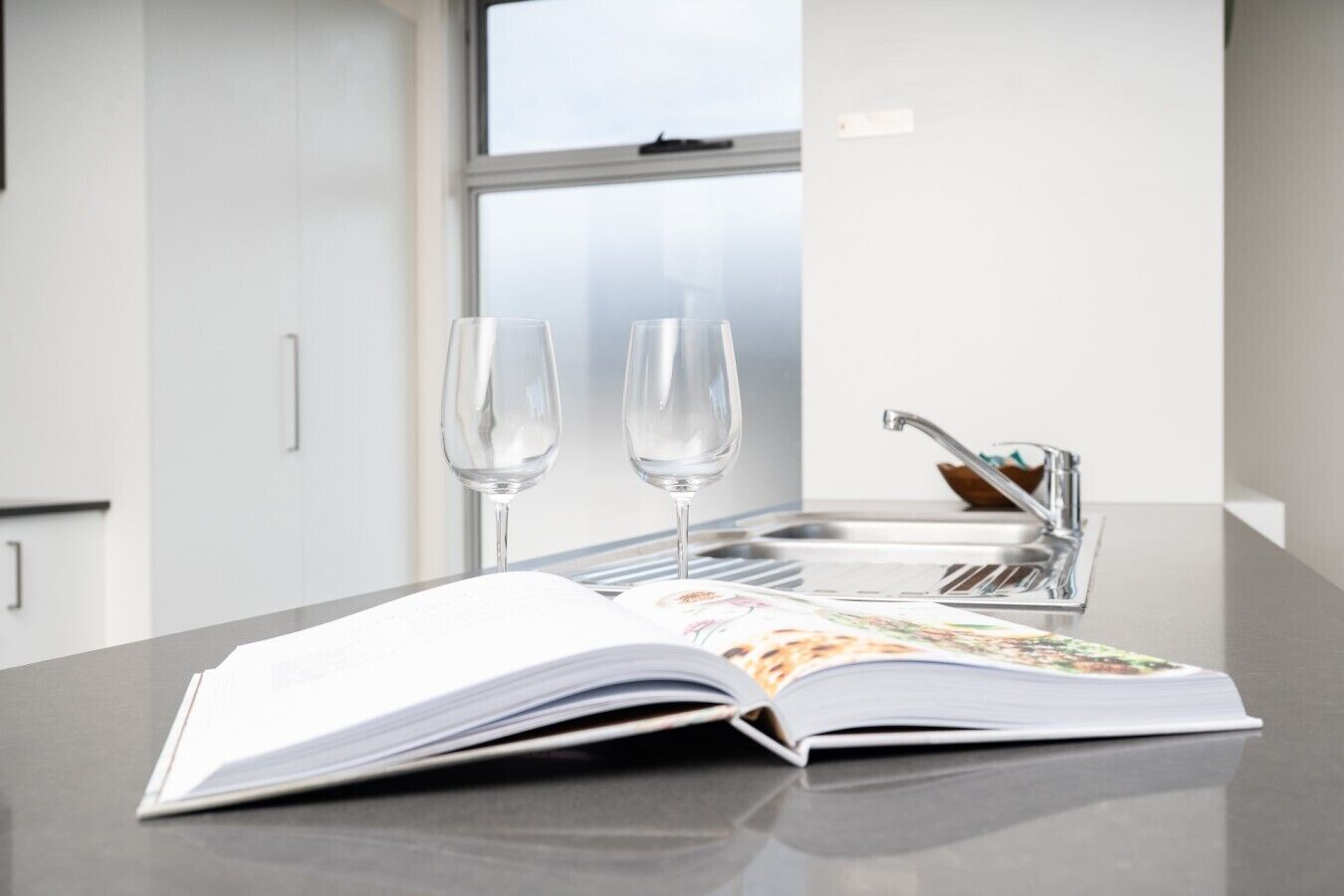A kitchen counter with an open magazine, two empty wine glasses, and a modern faucet.