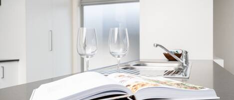 A kitchen counter with an open magazine, two empty wine glasses, and a modern faucet.