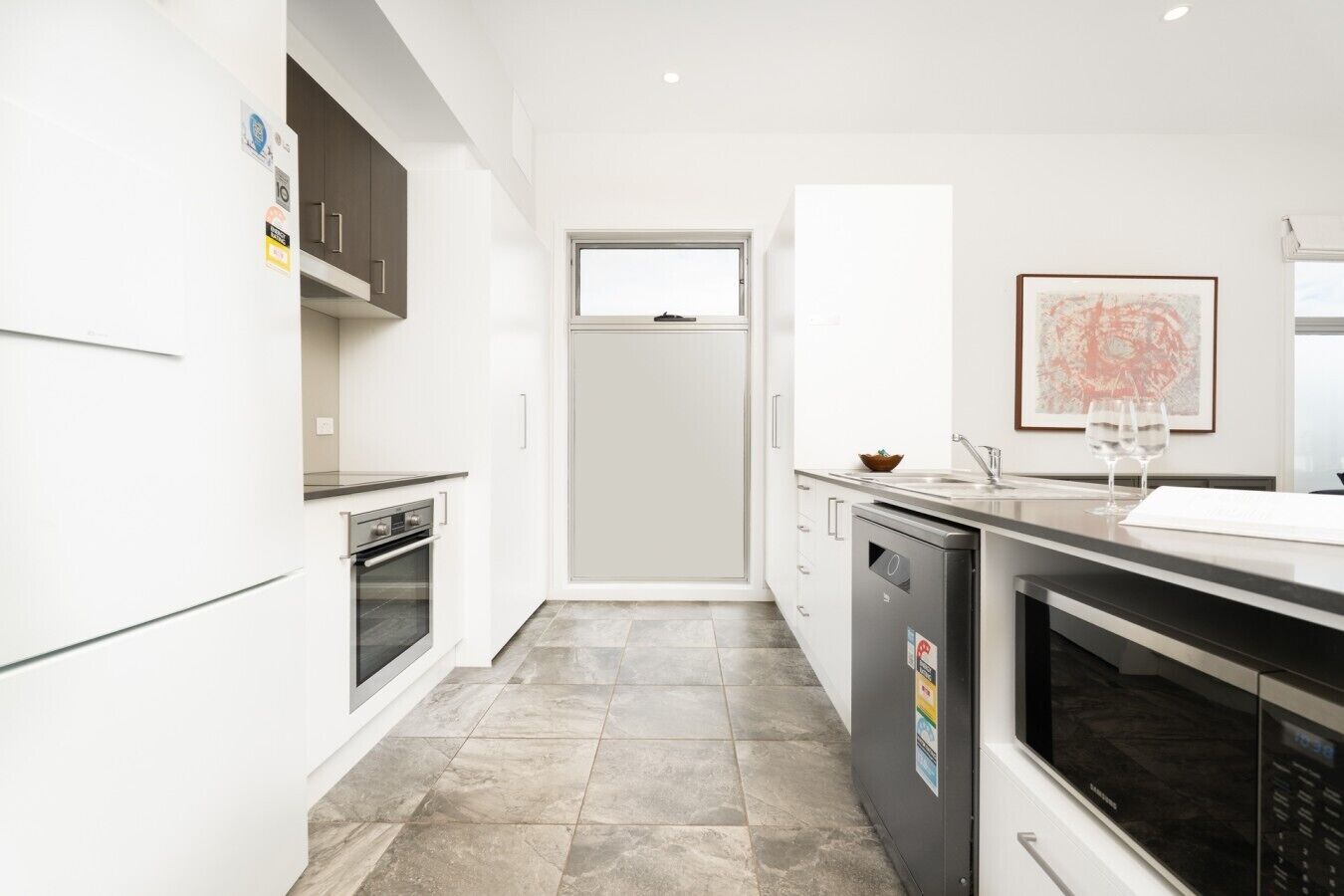 A modern kitchen with white cabinetry, a built-in oven, a dishwasher, and a window above the sink.