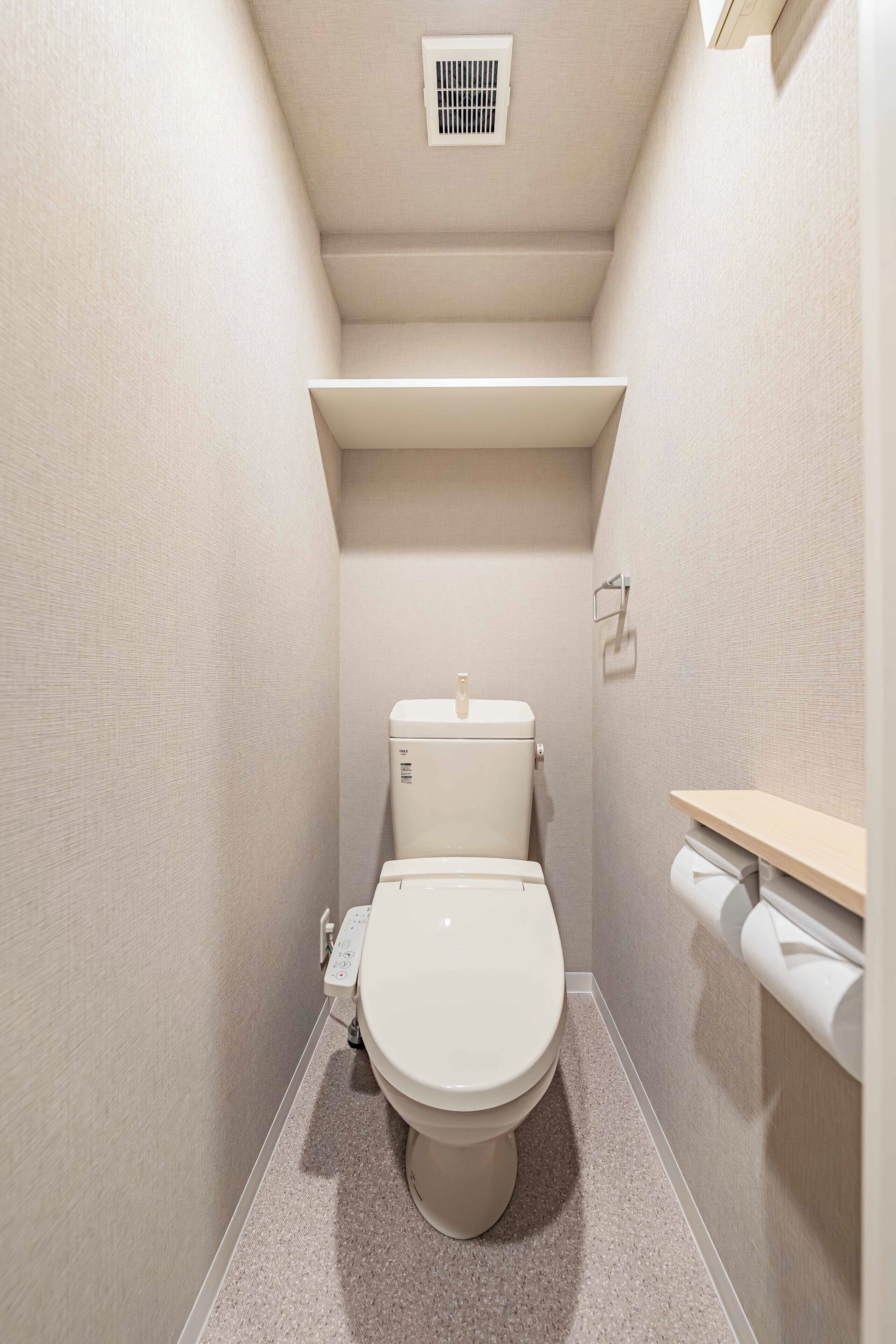 Ein kleines Badezimmer mit Toilette, Ablage über der Toilette und Lüftung im Deckenbereich.