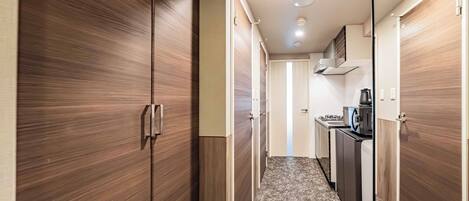 A hallway with wooden wardrobes, a kitchen area with a stove, and a microwave.