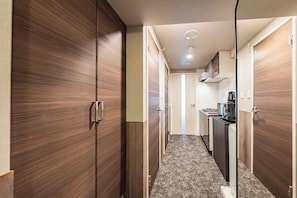 A hallway with wooden wardrobes, a kitchen area with a stove, and a microwave. - Apartment Hotel 11 Kuromon 8 (Osaka-shi)