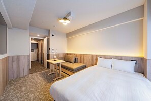 A hotel room with a large bed, a small table, a sofa, and a hallway leading to a bathroom. - Apartment Hotel 11 Kuromon 8 (Osaka-shi)