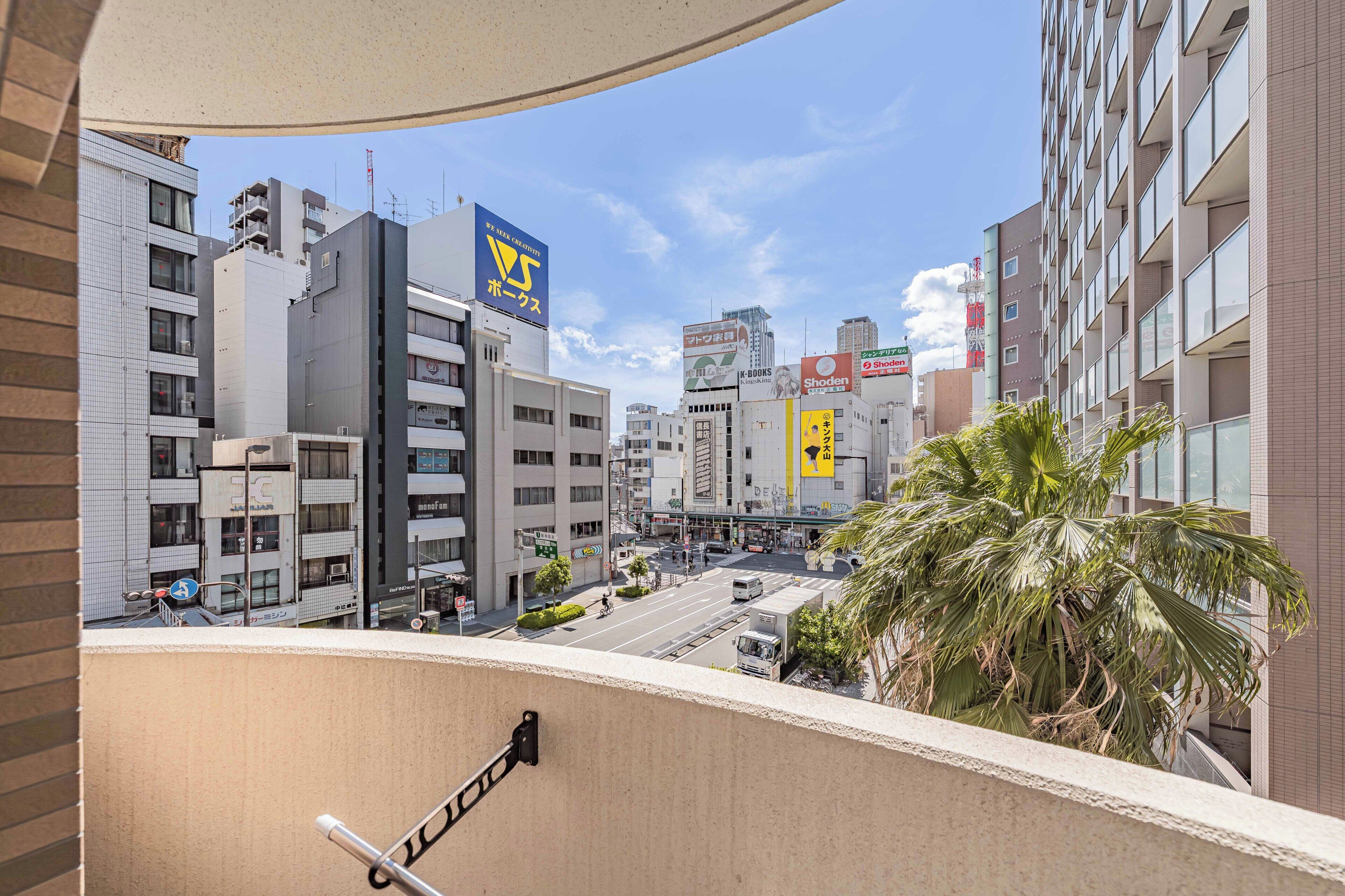 A cityscape with modern buildings, a clear sky, and a palm tree in the foreground.