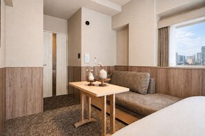 A hotel room with a bed, a sofa, a small table with decorative items, a window with a city view, and a door. - Apartment Hotel 11 Kuromon 8 (Osaka-shi)