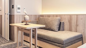 A modern hotel room with a wooden wall panel, a sofa, a small table with a vase, and a door with a handle. - Apartment Hotel 11 Kuromon 8 (Osaka-shi)